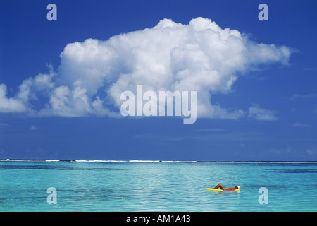 Donna galleggianti in un sogno sul materasso ad aria tra aqua chiare acque blu e bianco delle nuvole Foto Stock