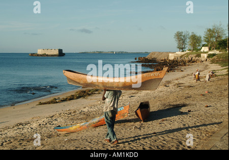 Un pescatore del Mozambico porta il suo scavato canoa sulla sua testa verso la riva di Ilha de Mozambico, Sud Africa. Foto Stock