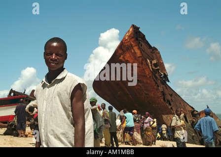 Un giovane uomo guarda la telecamera su Beira's Beach Dove grandi naufragio domina il paesaggio. Beira, Mozambico, Africa Foto Stock