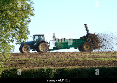 Il trattore e il rimorchio diffusione muck sul set aside campo prima il reseeding Foto Stock