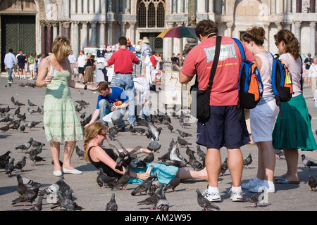 Giovane donna getta a terra con piccioni sul suo stomaco Mangiare chicchi di mais in Piazza San Marco Foto Stock