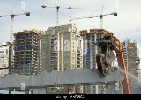 Demolizione di un edificio utilizzando un frantumatore di calcestruzzo con nuova costruzione in background Foto Stock