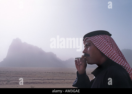 Giordano per uomo che indossa una keffiyah un tradizionale araba velo e fumare una sigaretta Wadi Rum Giordania Foto Stock