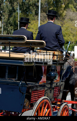 Due cocchieri guida un carrello barouche durante il Siviglia Fiera di Primavera, Siviglia, Andalusia, Spagna. Foto Stock