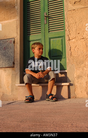 Ragazzo seduto su passi nel portale in sole serale Alcudia Maiorca Foto Stock