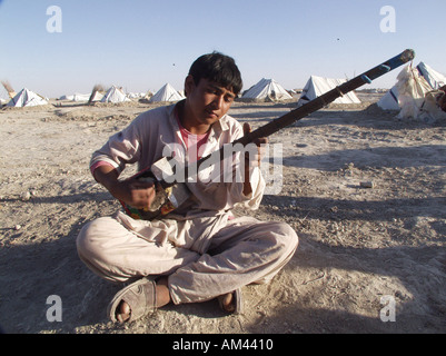 Gli sfollati interni in IDP camp Madreseh intorno a Zaranj Afghanistan giovane giocando tanbor fatti a mano Foto Stock