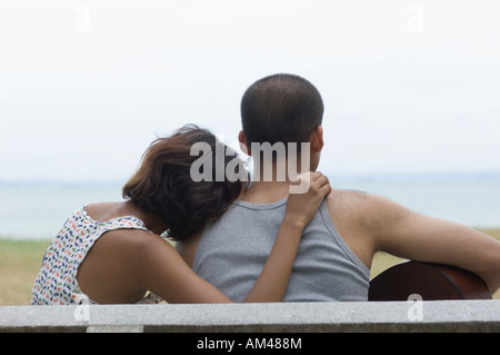 Vista posteriore di un giovane uomo seduto con il suo amico e di suonare una chitarra Foto Stock