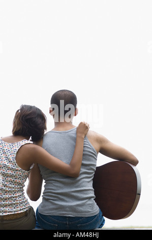 Vista posteriore di un giovane uomo seduto con il suo amico e di suonare una chitarra Foto Stock