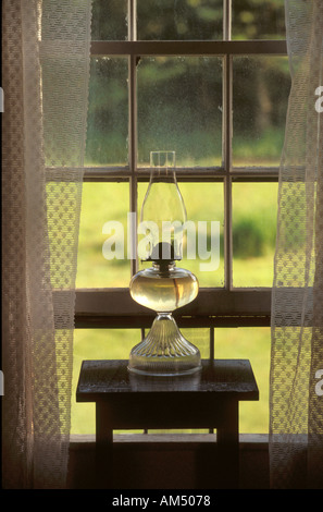 Un vetro trasparente lampada ad olio in home finestra con tende di pizzo. Foto Stock