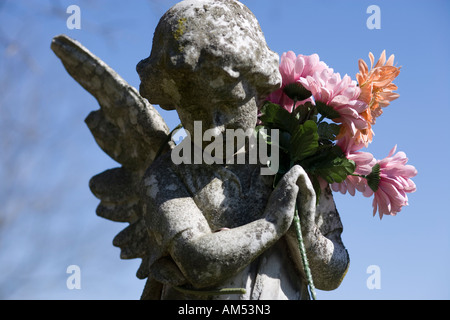 Angelo di pietra con fiori di plastica in un cimitero di noi. Messa a fuoco poco profonde. Foto Stock