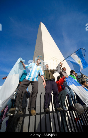 Appassionati di calcio allietare il bilanciamento pericolosamente su un forte recinto intorno all'Obelisco di Buenos Aires. Foto Stock