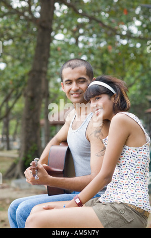 Giovane uomo seduto con la sua fidanzata e di suonare una chitarra Foto Stock