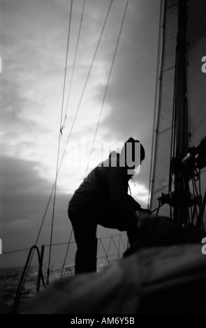 Yacht membro di equipaggio regola rigging all'alba nel mare d' Irlanda a metà strada tra la costa di Wexford e Milford Haven in Galles Foto Stock