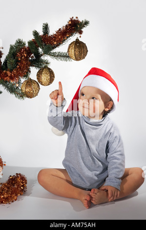 Piccolo Ragazzo giocoso sotto l albero di Natale ramo su sfondo chiaro non isolato Foto Stock