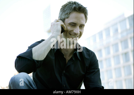 Uomo in camicia nera a parlare sul suo cellulare Foto Stock