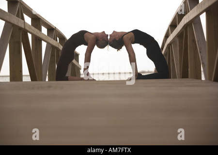 Due donna indietro pratica yoga di piegatura pongono toccando le loro teste insieme Foto Stock