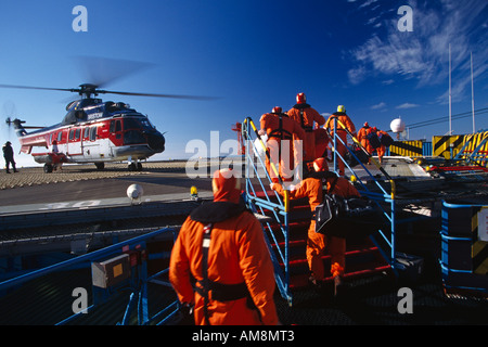 Offshore Oil Platform personale cambiamento di equipaggio imbarco elicottero sulla piattaforma petrolifera nel Mare del Nord con Puma elicottero in background Foto Stock