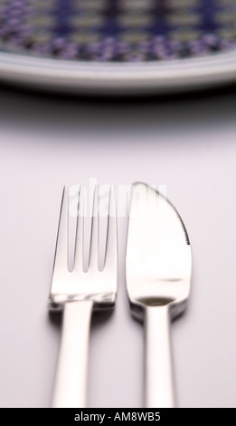 Immagine astratta di un coltello e forchetta affiancati su una superficie bianca con il bordo curvo di una piastra di sommità del imag Foto Stock