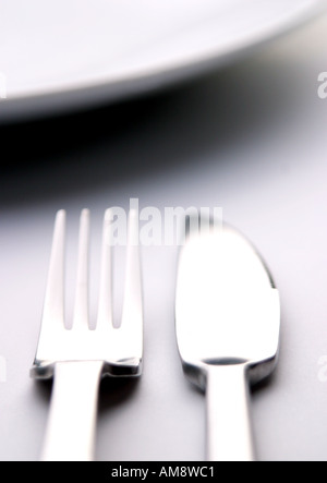 Immagine astratta di un coltello e forchetta affiancati su una superficie bianca con il bordo curvo di una piastra di sommità del imag Foto Stock