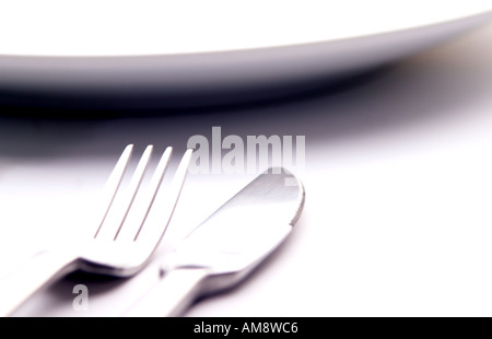 Immagine astratta di un coltello e forchetta affiancati su una superficie bianca con il bordo curvo di una piastra di sommità del imag Foto Stock