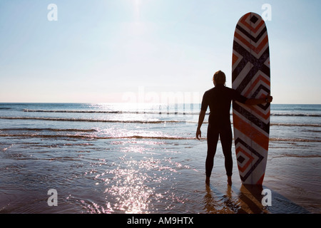 Uomo in piedi sulla spiaggia con la tavola da surf. Foto Stock
