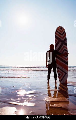 Uomo in piedi sulla spiaggia con la tavola da surf. Foto Stock