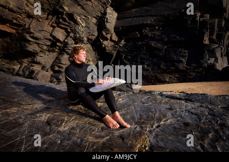 Uomo seduto sulla grande roccia in neoprene con la tavola da surf sul giro. Foto Stock