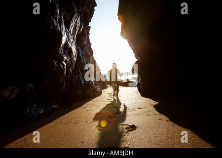 Donna che trasportano le tavole da surf attraverso rocce di grandi dimensioni. Foto Stock