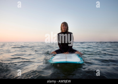 Donna seduta sulla tavola da surf in acqua sorridente. Foto Stock