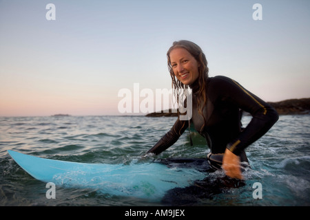 Donna seduta sulla tavola da surf in acqua sorridente. Foto Stock