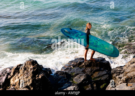 Donna in piedi su rocce di grandi dimensioni con una tavola da surf sorridente. Foto Stock