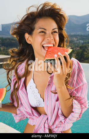 Donna energica con sorriso mangia anguria da piscina all'esterno. Foto Stock