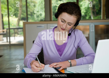 Una giovane donna che indossa una cuffia telefonica mentre lavora a una scrivania Foto Stock
