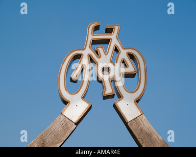 Cielo blu e la scultura di bicicletta su arch al di sopra di ingresso al percorso ciclabile lungo la Cob Porthmadog Gwynedd North Wales UK Foto Stock