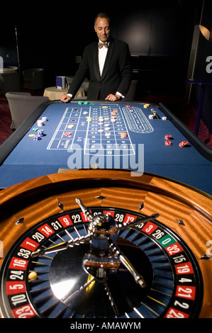 Ben vestito uomo in piedi al tavolo della roulette Foto Stock