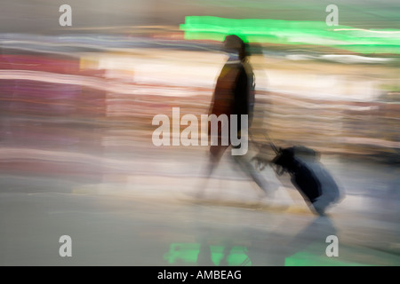 Passando attraverso un intenzionalmente immagine sfocata di una donna che si spostano rapidamente se un aeroporto tirando una valigia su ruote dietro Foto Stock