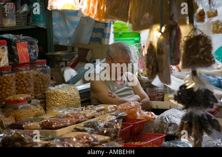 Un anziano titolare di stallo si appoggia alla sua bancarella vendendo generi alimentari essiccati nel mercato di Wanchai Hong Kong Foto Stock