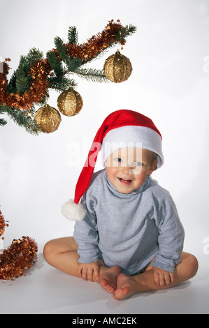 Piccolo Ragazzo giocoso sotto l albero di Natale ramo su sfondo chiaro non isolato Foto Stock