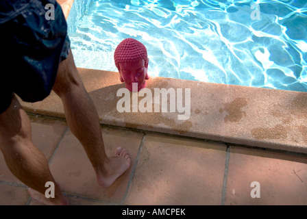 Un uomo si erge accanto al buddha rosa testa dal lato di una piscina sotto il sole Foto Stock