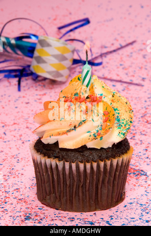 Un solitario cupcake al cioccolato con giallo glassa di turbolenza si siede su una rosa di sfondo di partito con una celebrazione fischio Foto Stock