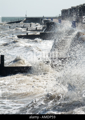 Persone che camminano in sea spray lungo mare di calcestruzzo a parete e promenade tempesta di vento mare mosso le percosse costiere le difese di mare lungo la costa di Essex England Regno Unito Foto Stock