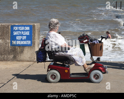 Lungomare lungomare donna matura seduta su scooter motorizzati per disabili che guarda Walton sull'alta marea sul Naze Essex Inghilterra Regno Unito Foto Stock