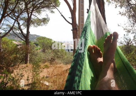 I piedi di un uomo rilassante in un verde amaca messicana in collina che si affaccia sul mar Mediterraneo, Costa Brava, Spagna. 2006. Foto Stock