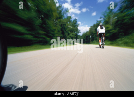 Vista posteriore dell'uomo equitazione Bicicletta su strada attraverso gli alberi Foto Stock