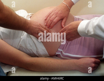 Un medico e un potenziale padre a sentire e ad esaminare la gravidanza di una donna di bump, ambulatorio medico, Londra, Regno Unito. Foto Stock