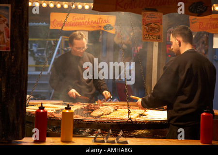 Due uomini in un fast food vendita di carne di stallo rostbratwurst cook e bistecca su un enorme open grill spandau mercatini di Natale Berlino Foto Stock