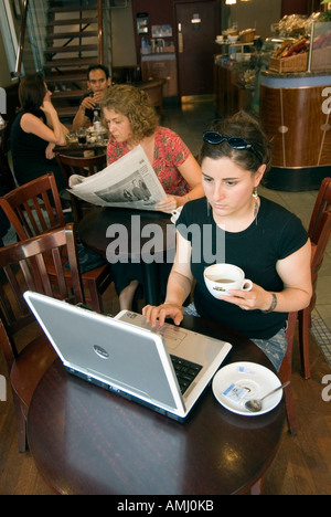 Giovane donna navigando in internet su un computer portatile in un caffè nero, London, England, Regno Unito Foto Stock