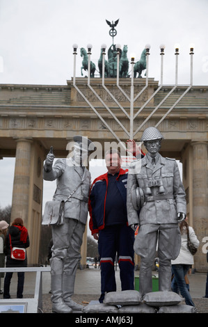 Turista che posano per una fotografia con verniciato argento street intrattenitore vestito come est guardia tedesco Porta di Brandeburgo a Berlino Foto Stock