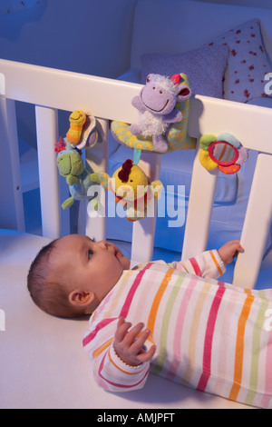 Un bambino giace sulla sua schiena in un lettino in un vivaio e guarda a una luce notturna toy Foto Stock