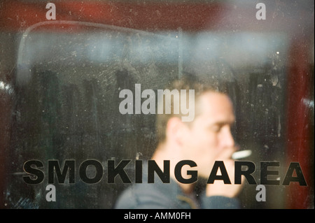 Un uomo di fumare in un rifugio di fumare a seguito del divieto di fumo Foto Stock